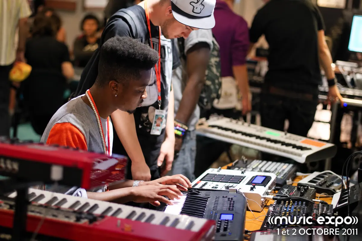 Un jeune musicien essaie un clavier sur un stand d’instruments, entouré d’autres visiteurs.